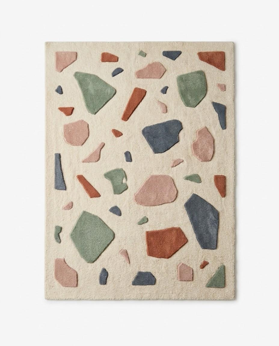 Terrazzo pattern area rug featuring scattered geometric stone shapes in pastel pink, sage green, slate blue, and terracotta on a cream background.