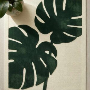 Tropical Monstera Leaf Rug featuring large botanical deep green leaves on a clean cream background next to an indoor plant.
